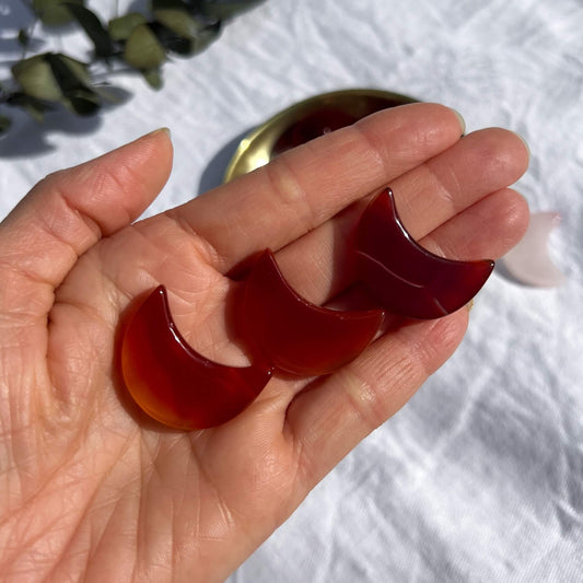 Three mini deep red carnelian crystal moons displayed on an open hand