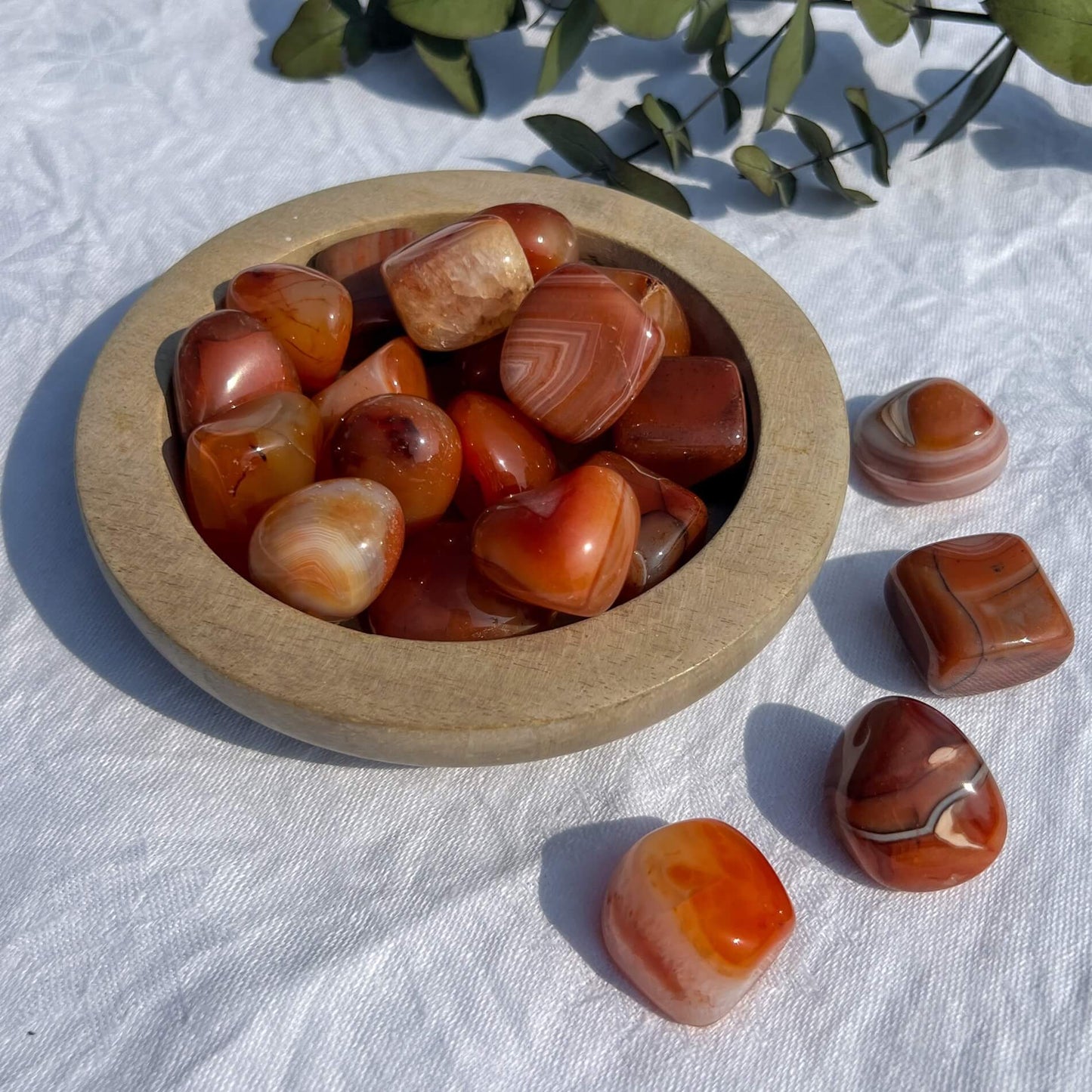 A wooden dish overflowing with large red and orange patterned carnelian crystal pebbles