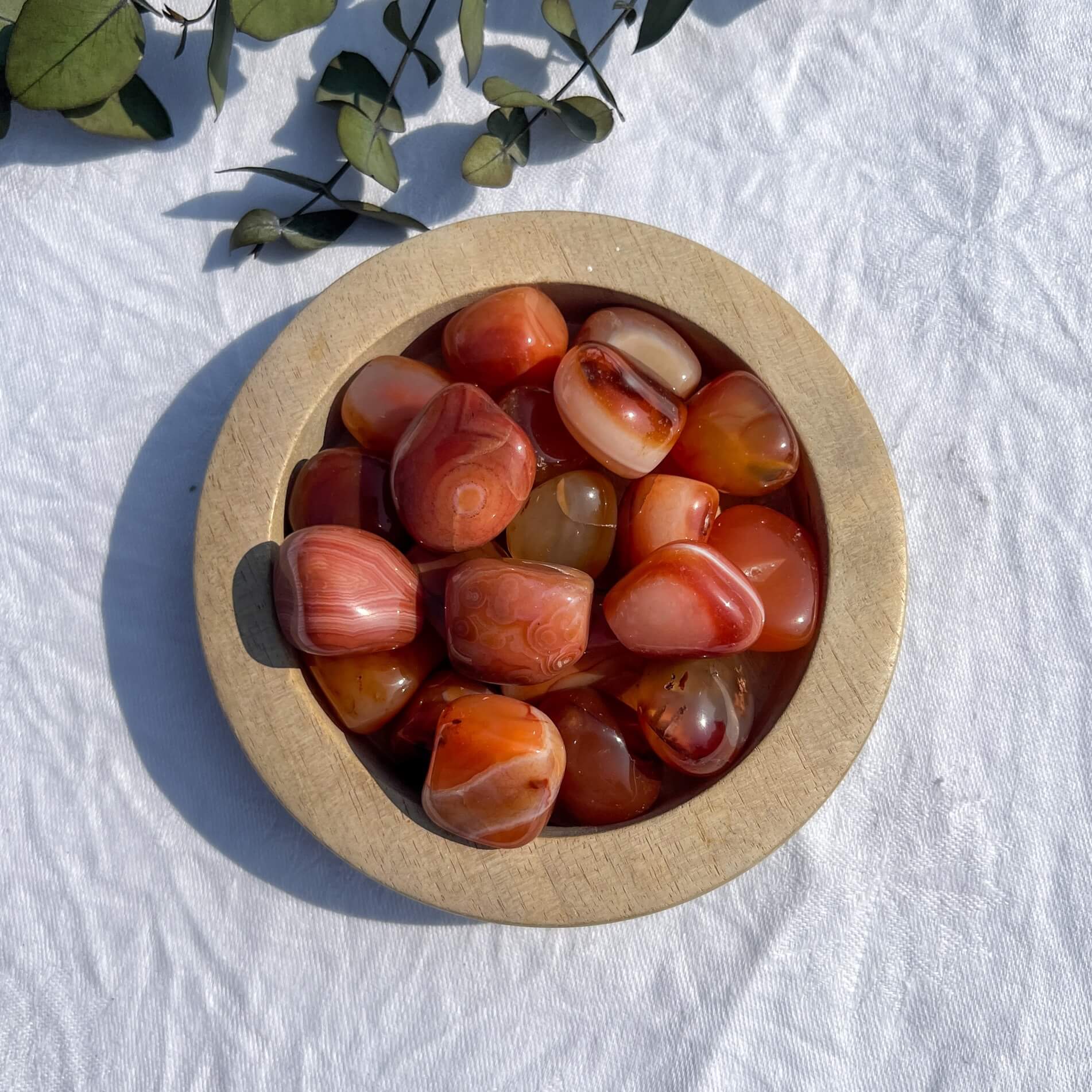 An aerial view of a wooden dish filled with  bright red, white and orange patterned extra large carnelian crystal tumblestones