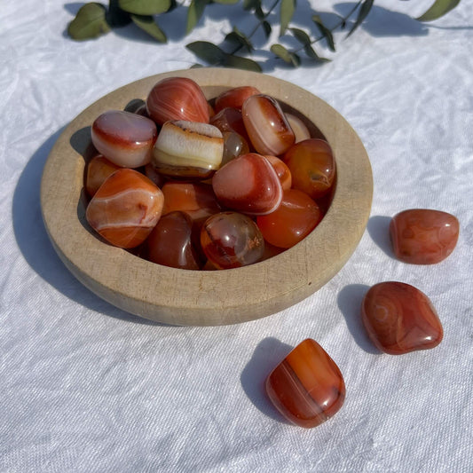 A wooden dish overflowing with bright red, white and orange patterned extra large carnelian crystal tumblestones