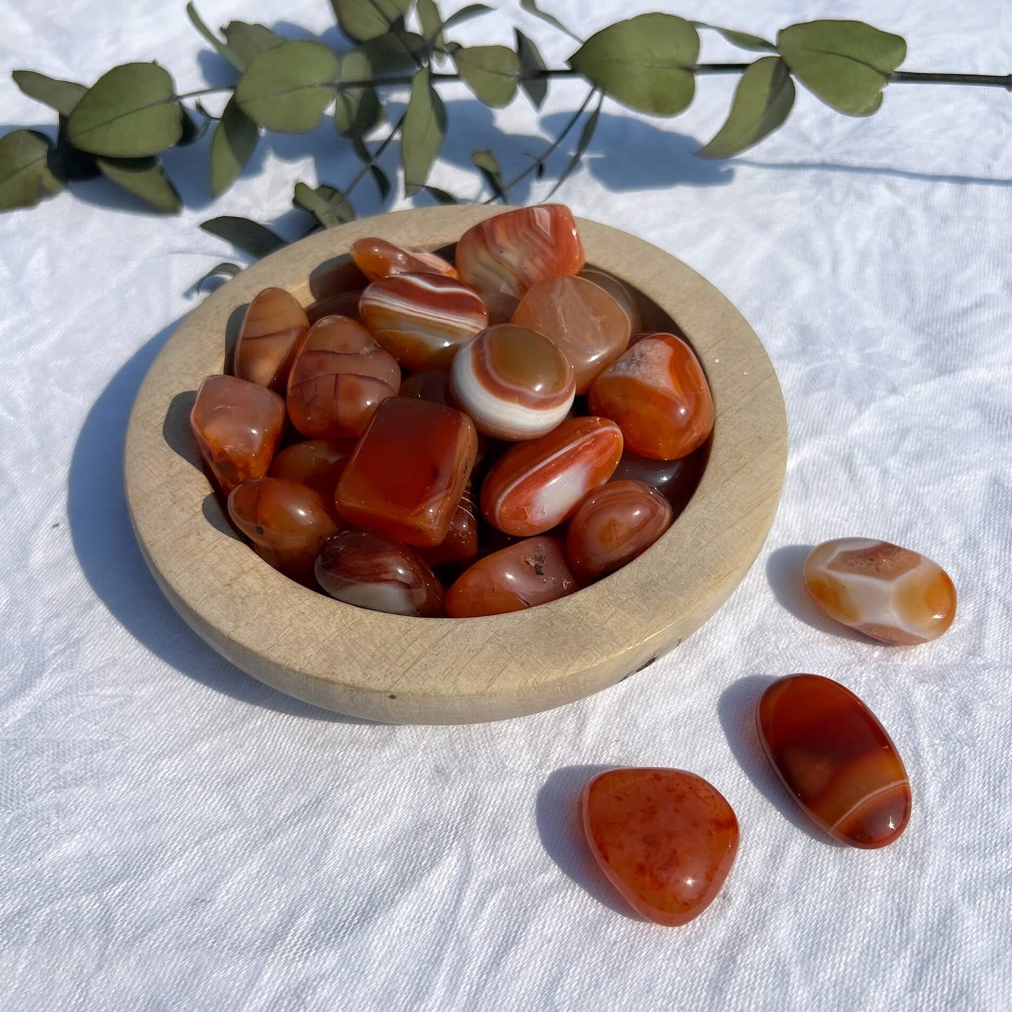 A wooden dish filled with vibrant red and orange patterned carnelian crystal tumblestones