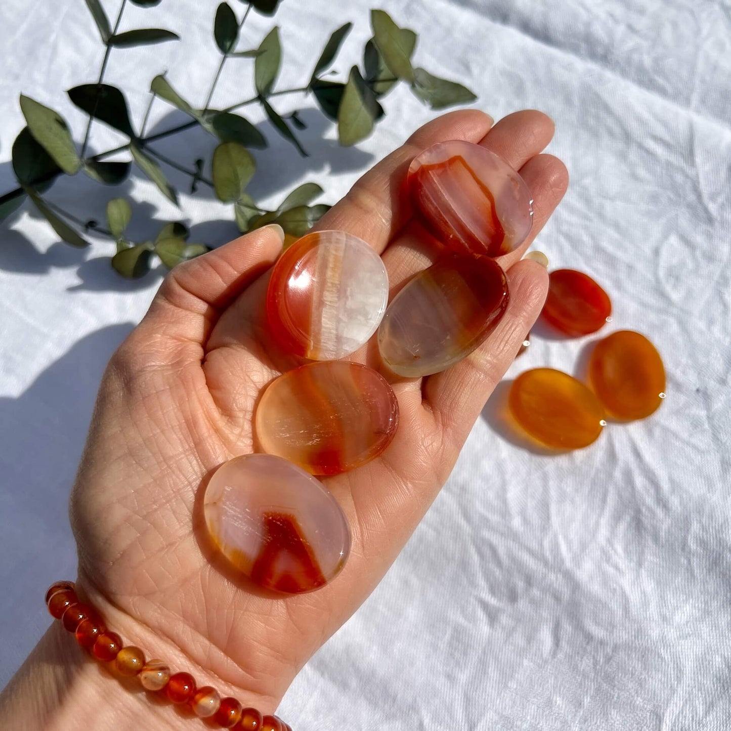 An outstretched hand holding four red and orange patterned oval carnelian crystal thumb stones