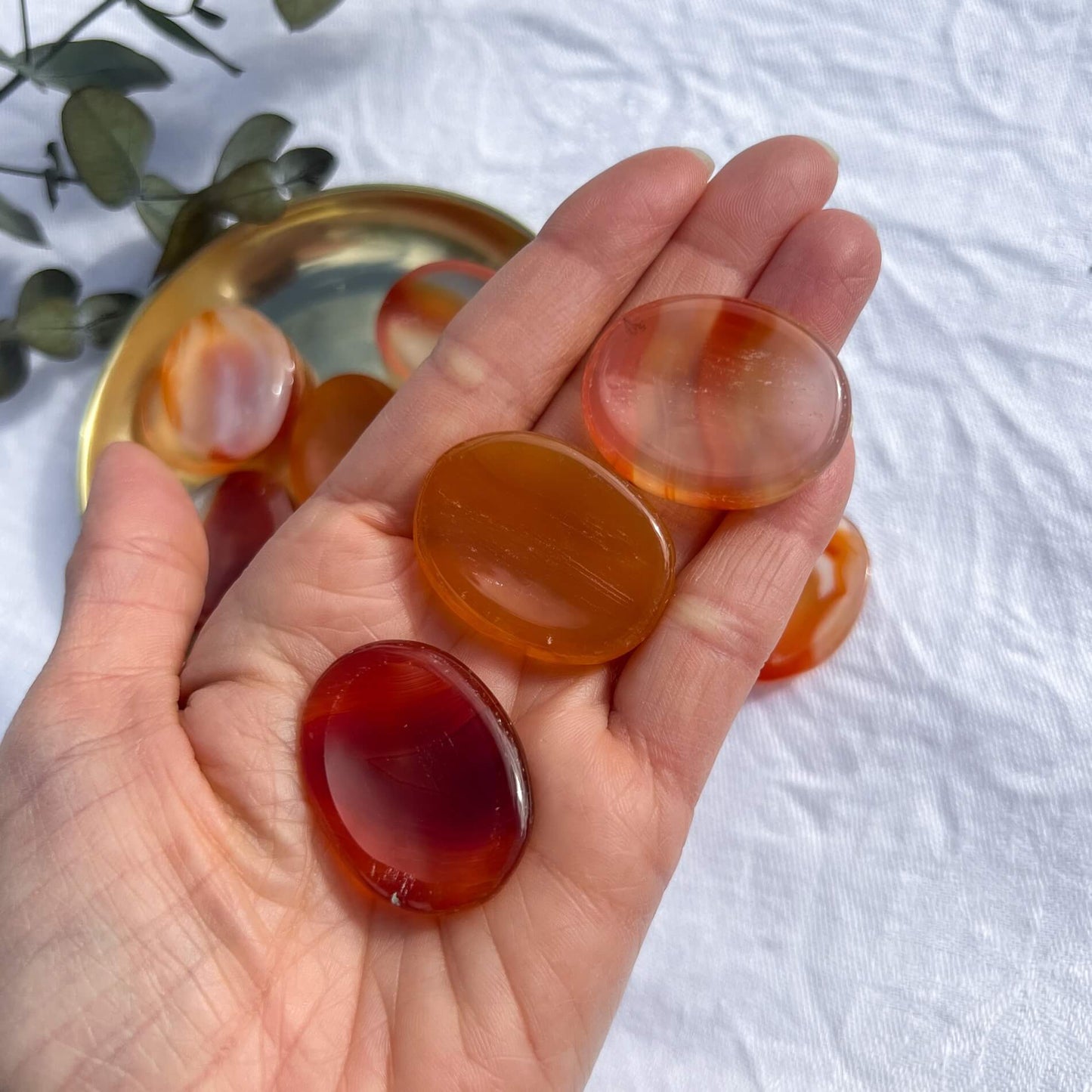 An outstretched hand holding four red and orange carnelian crystal worry stones