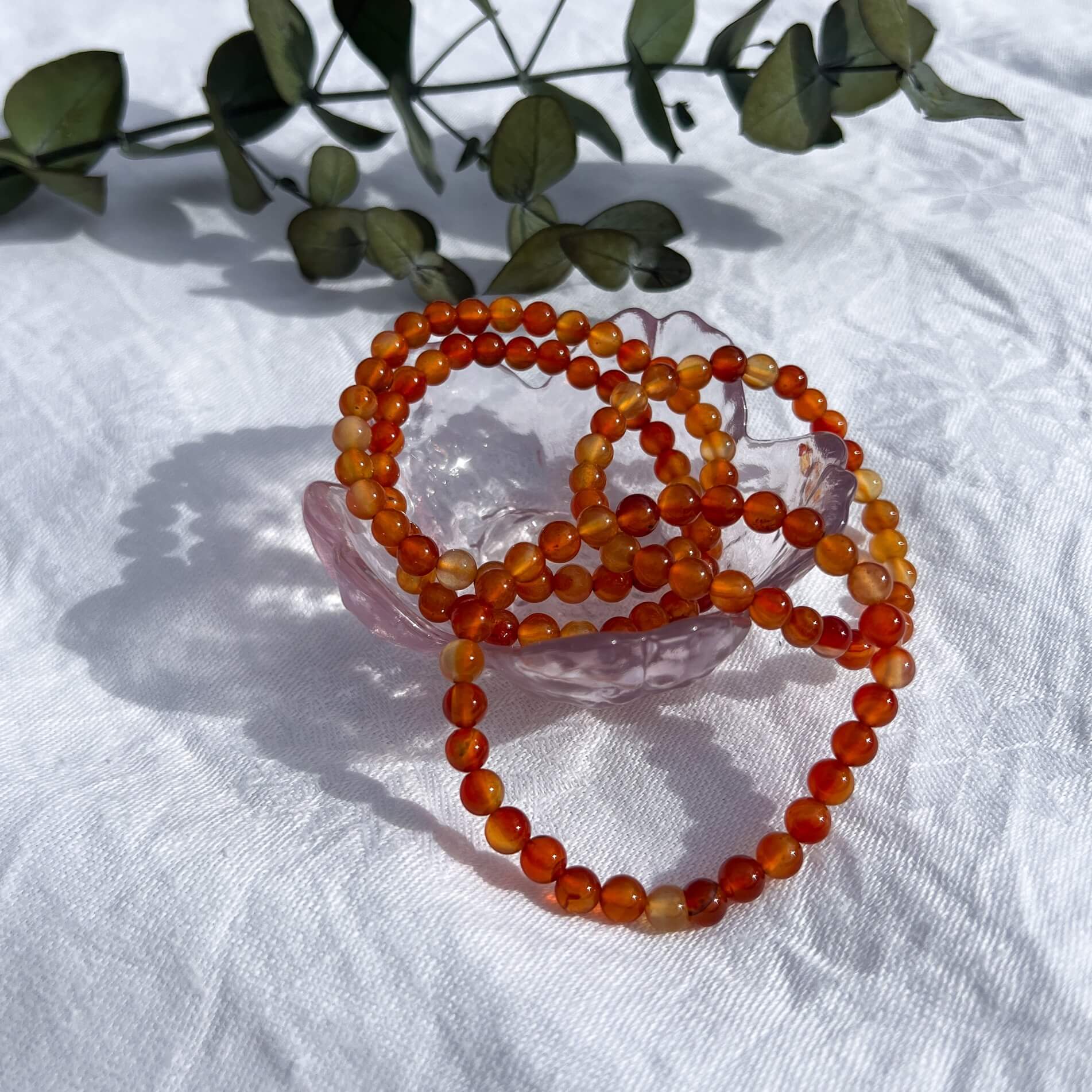 A glass trinket dish filled with vivid orange & red carnelian crystal bead bracelets