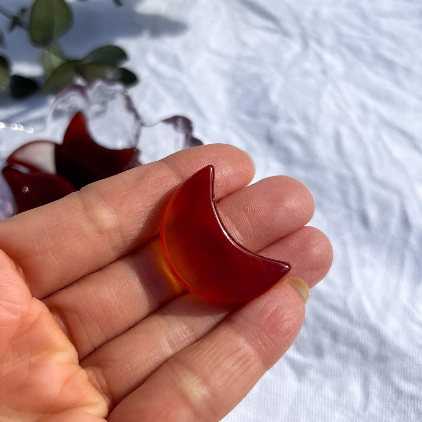 A small red carnelian crystal moon shown in an open hand