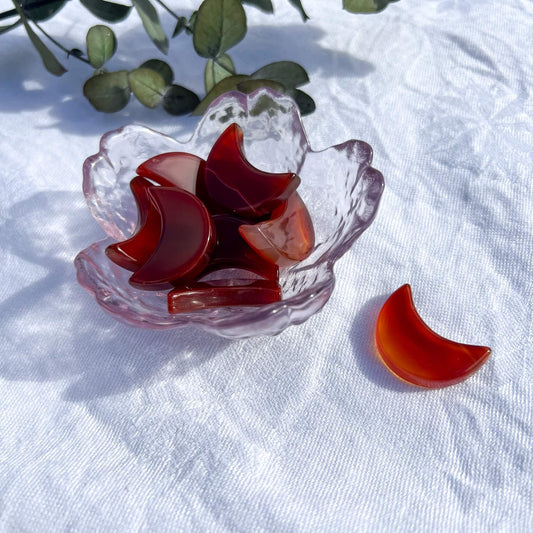 A small pink glass trinket dish filled with dark red carnelian crystal mini moons, with a vibrant red mini crystal moon in the foreground