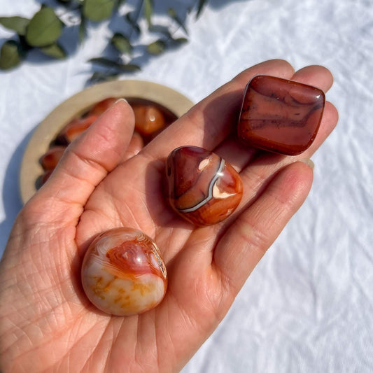 An open hand holding three large red and orange patterned carnelian crystal pebbles