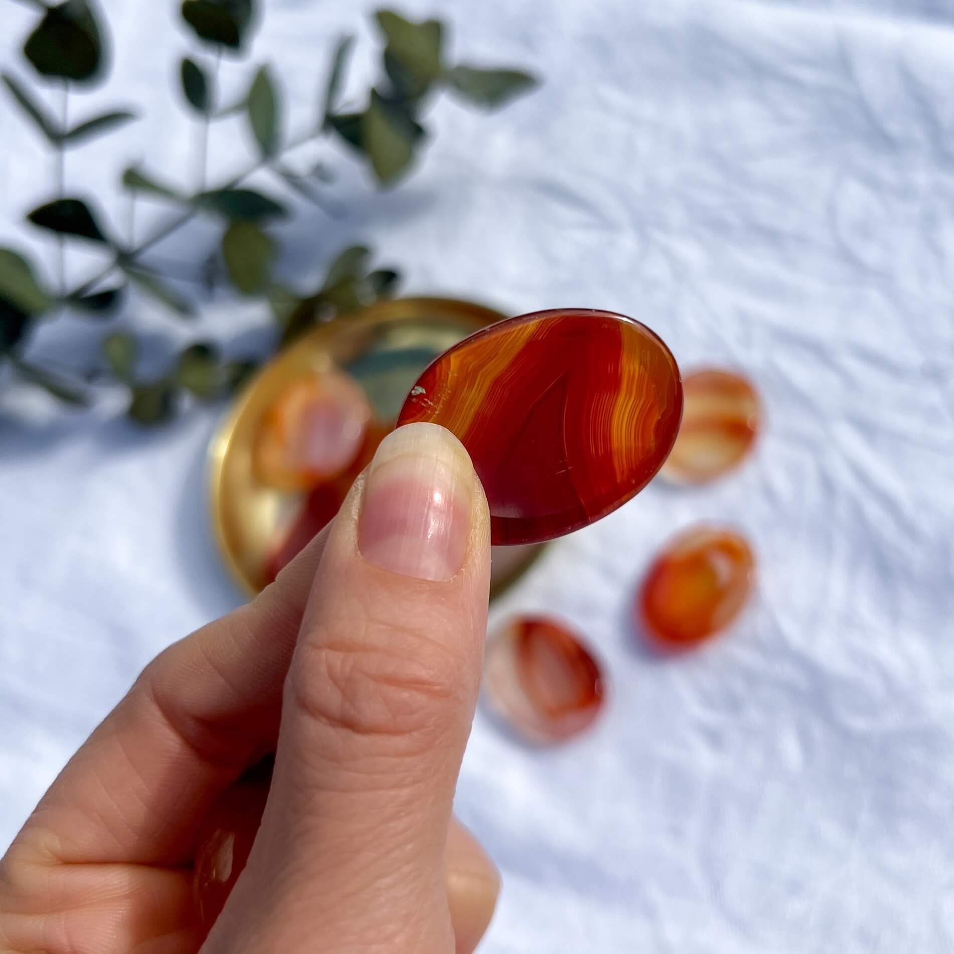 A patterned red carnelian crystal oval worry stone is held to camera between pinched fingers