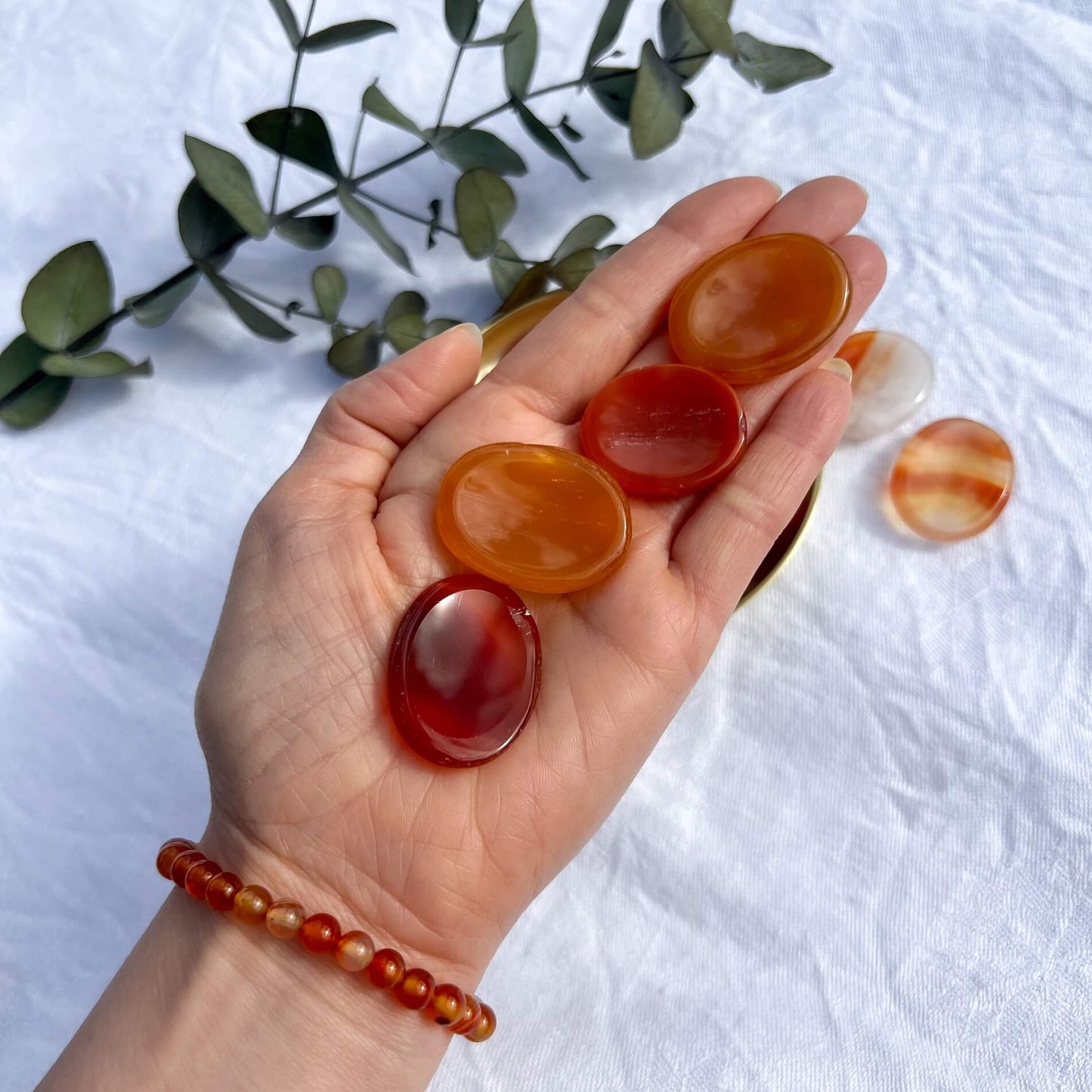 An outstretched hand holding four red and orange oval carnelian crystal thumb stones