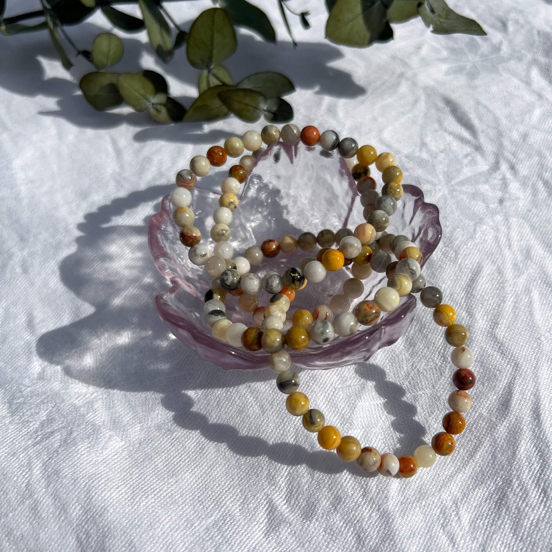 A glass dish filled with 3 yellow, white & amber coloured crazy lace agate crystal bead bracelets
