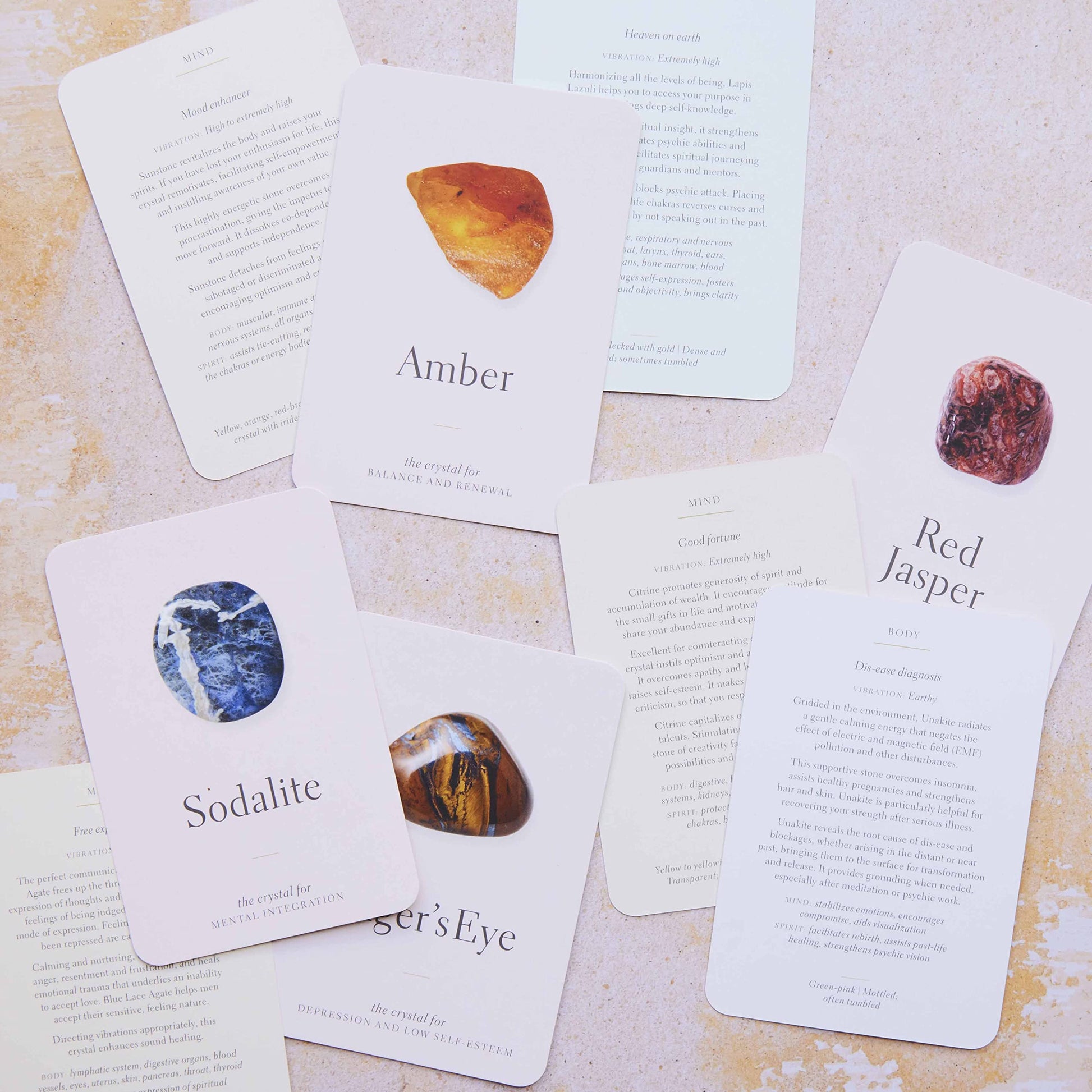 A spread of pale pink crystal cards with pictures of crystals on the front and their descriptions on the back, with sodalite, amber and red jasper visible.