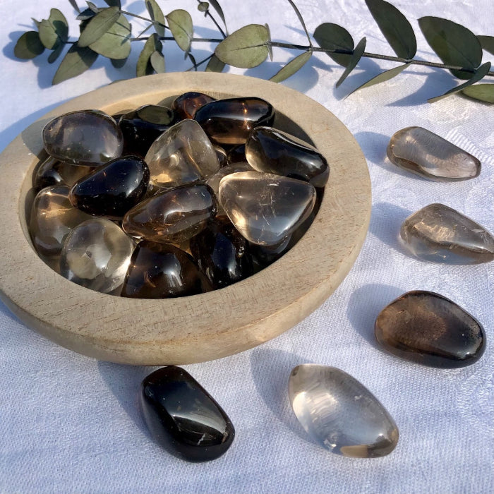 Wooden bowl full of dark brown smoky quartz crystals spilling onto table