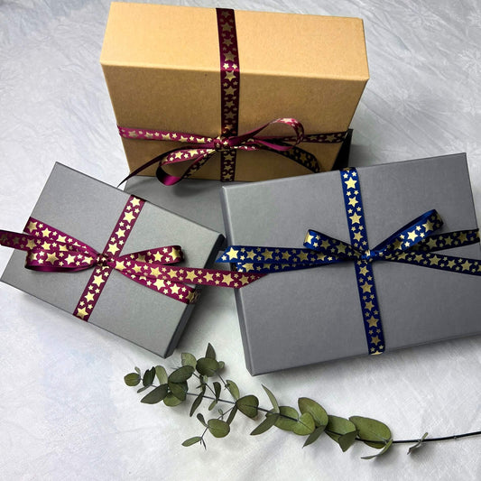 Three festive gift boxes tied in navy and burgundy ribbons covered in bright golden stars