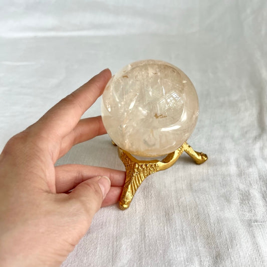 Gold vintage style small crystal sphere holder with a honey optical calcite sphere on top and hand for size reference