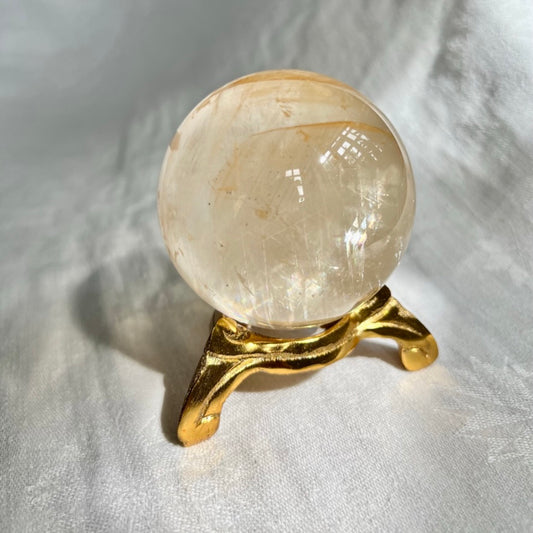 Vintage swirl style gold coloured crystal sphere holder with honey calcite sphere shiny in the afternoon sun
