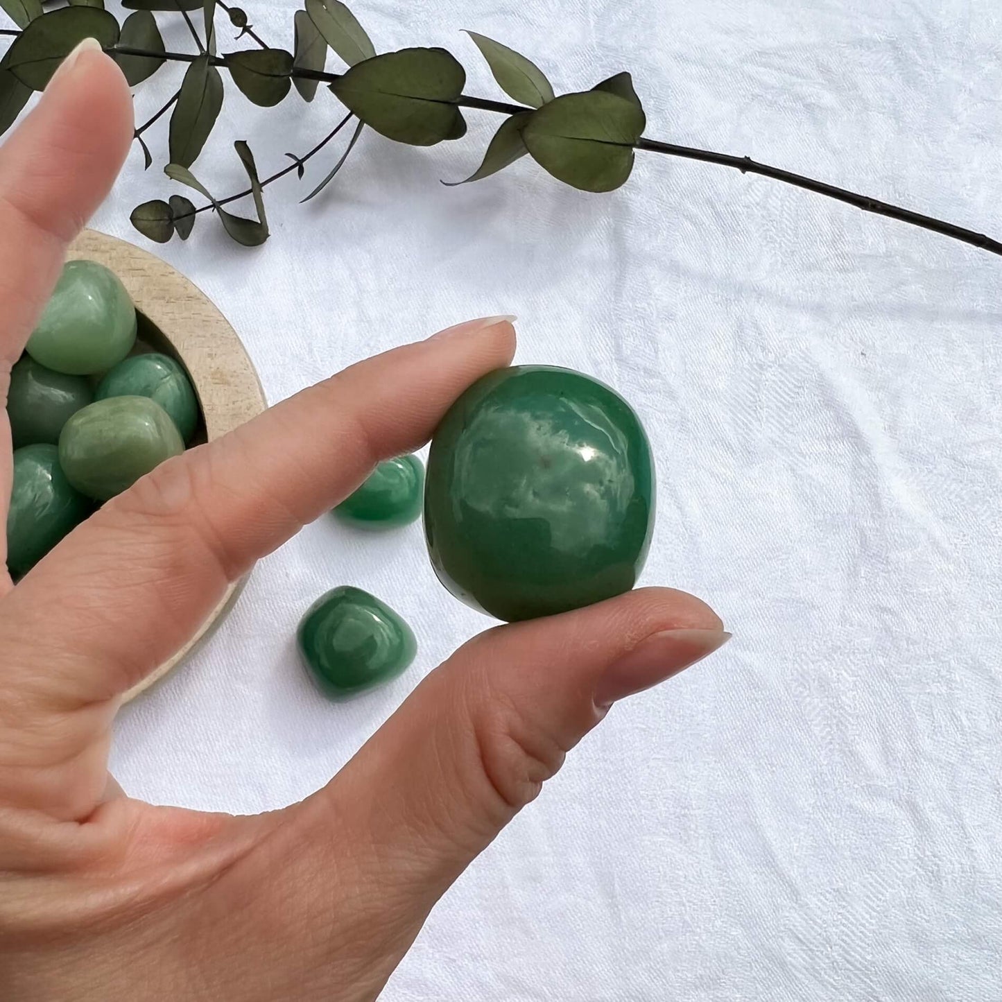A large glossy green aventurine crystal tumble stone held in pinched fingers