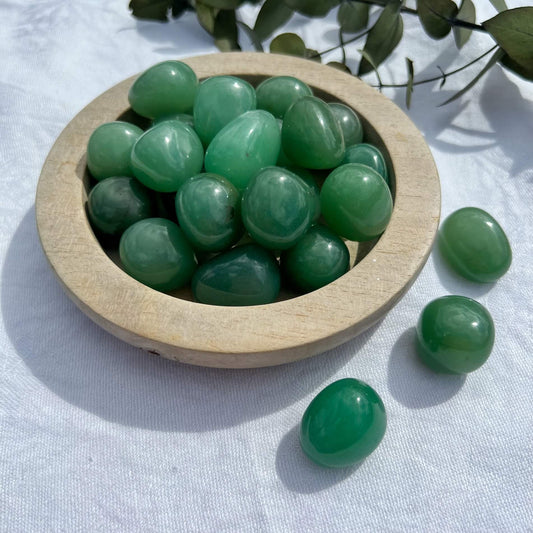 Glossy green aventurine crystal tumblestones displayed in a wooden dish