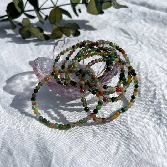 A glass trinket dish filled with multi-coloured green jasper crystal bead bracelets