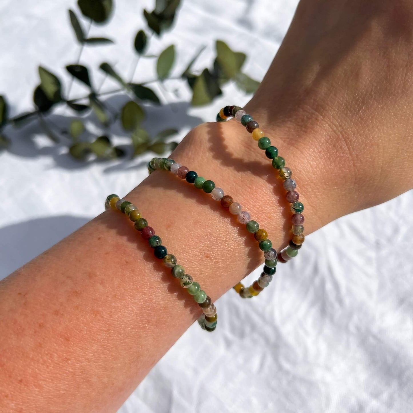 A woman's arm wearing three multi-coloured green jasper crystal bead bracelets