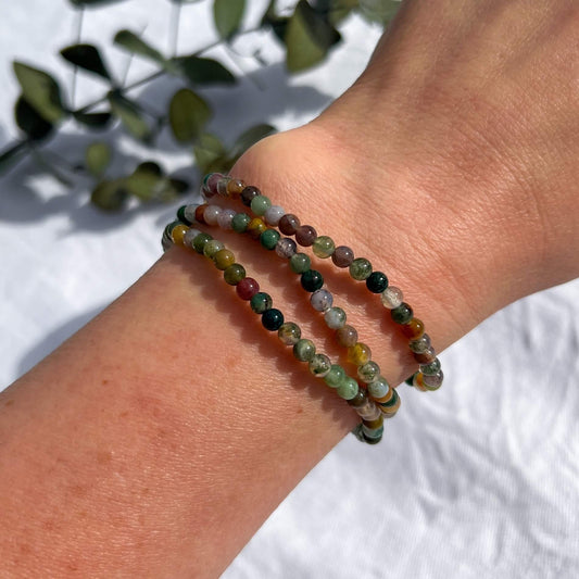 A woman's wrist wearing three green jasper crystal bead bracelets