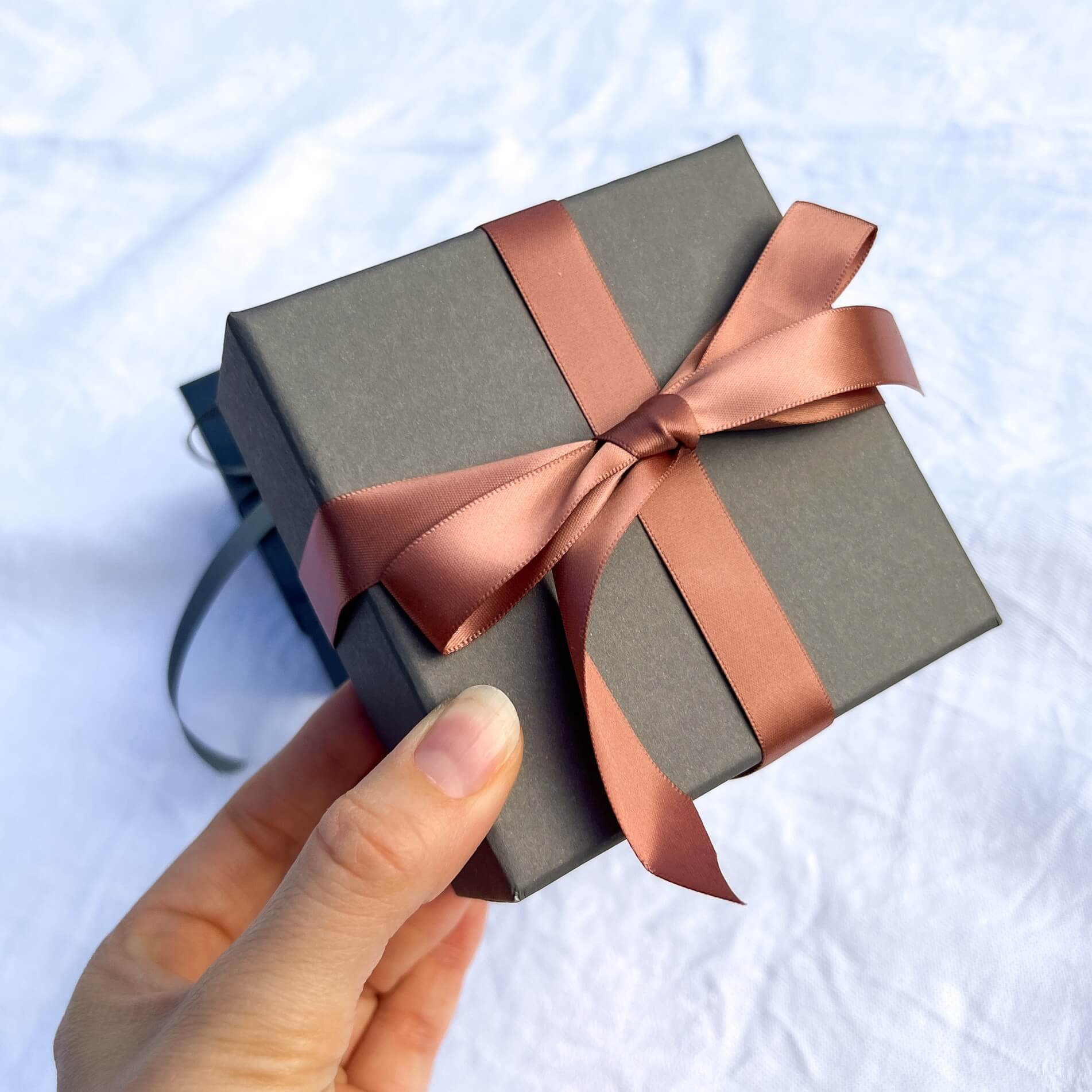 Luxury grey gift box tied in a rose gold pink ribbon held to camera