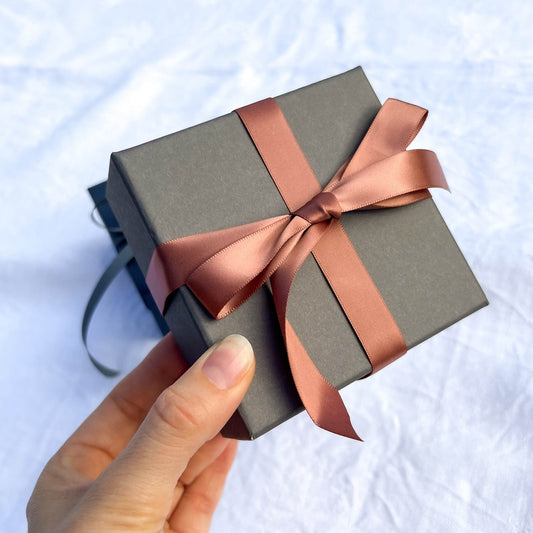 Luxury grey gift box tied in a rose gold pink ribbon held to camera