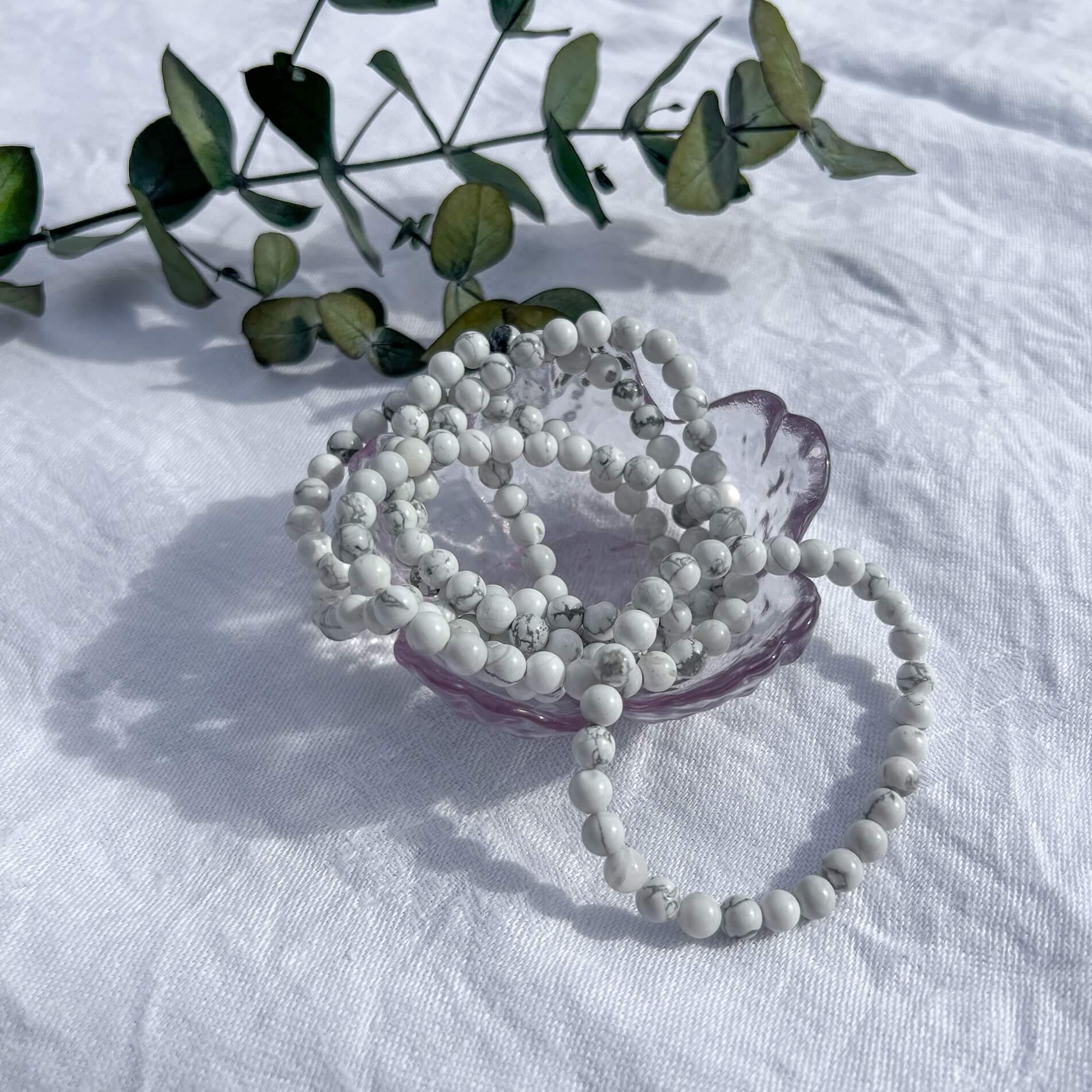 A glass trinket dish filled with white and grey marbled Howlite healing crystal bead bracelets