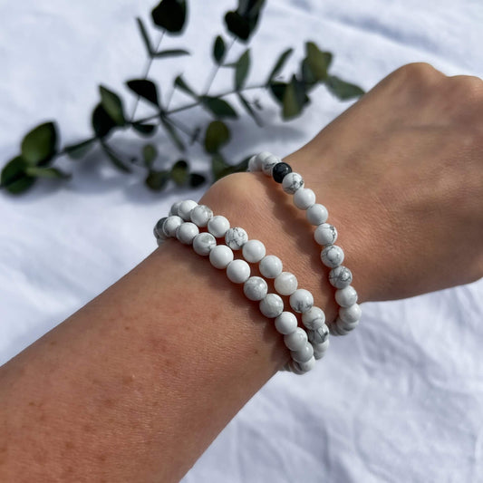 A woman's arm wearing three white and grey marbled Howlite healing crystal bead bracelets