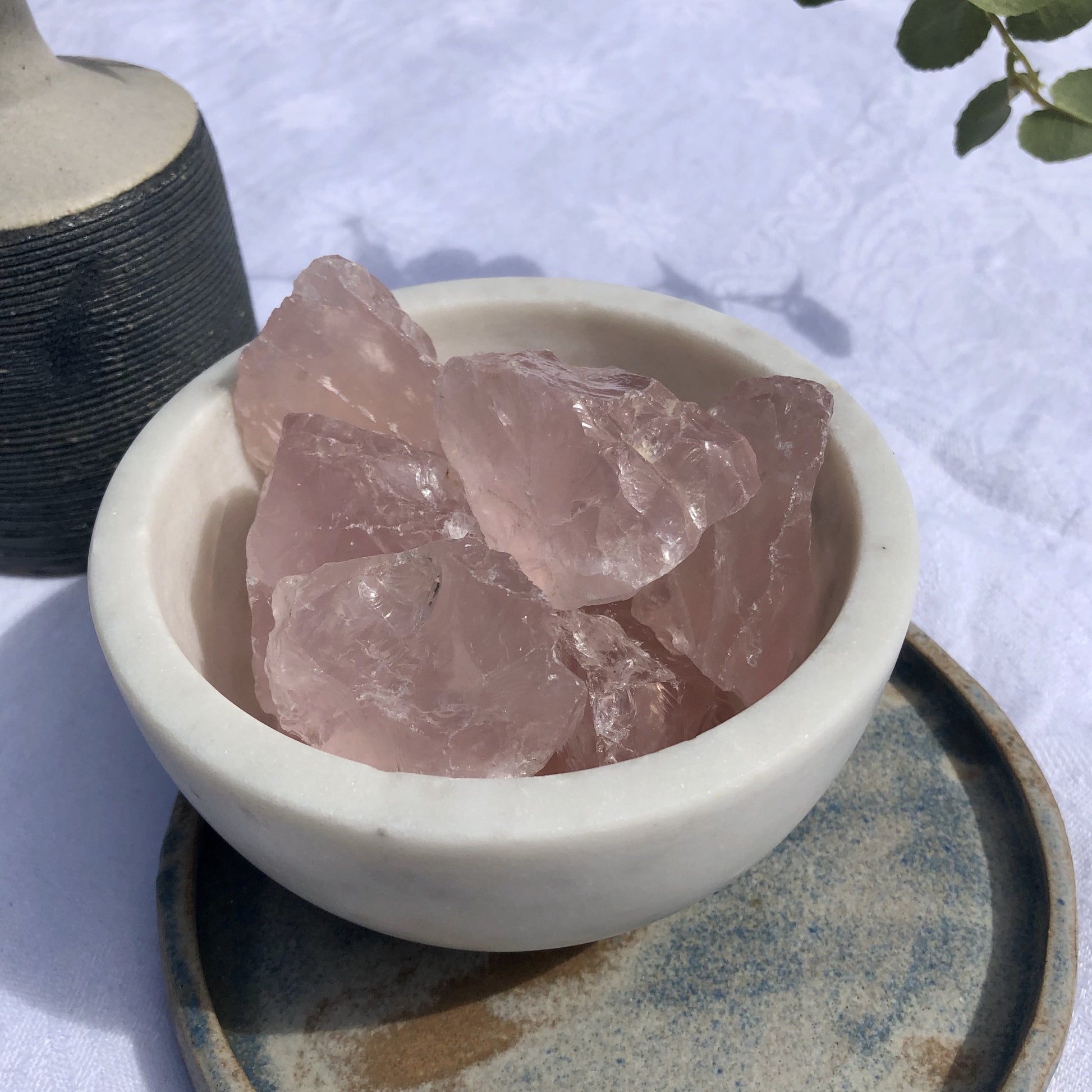 A white marble bowl of light pink gummy chunks of rose quartz crystal on a ceramic plate