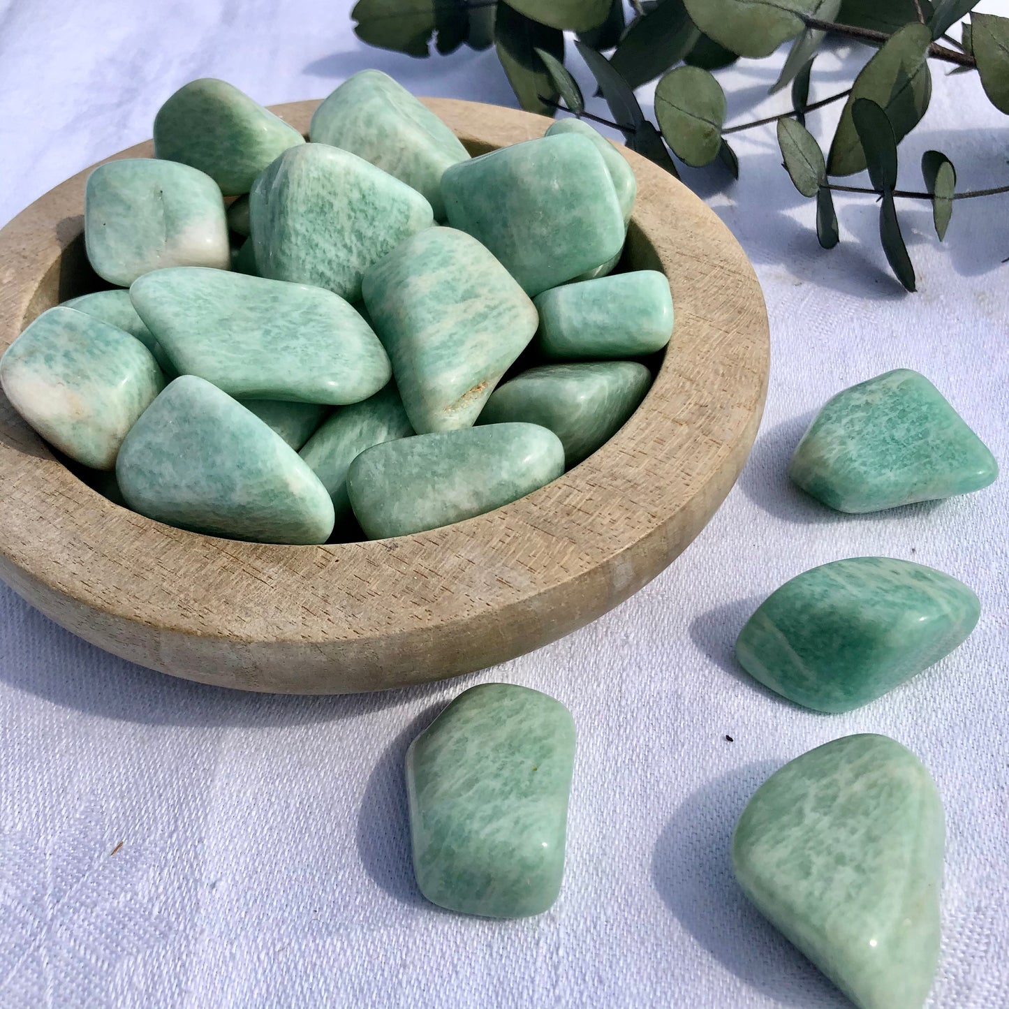 A shallow wooden dish filled with turquoise Amazonite tumble stones spilling onto the white table cloth