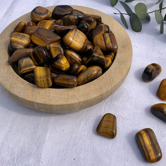 Ethically sourced flashy tigers eye crystal tumble stones in a wooden bowl on a white table cloth