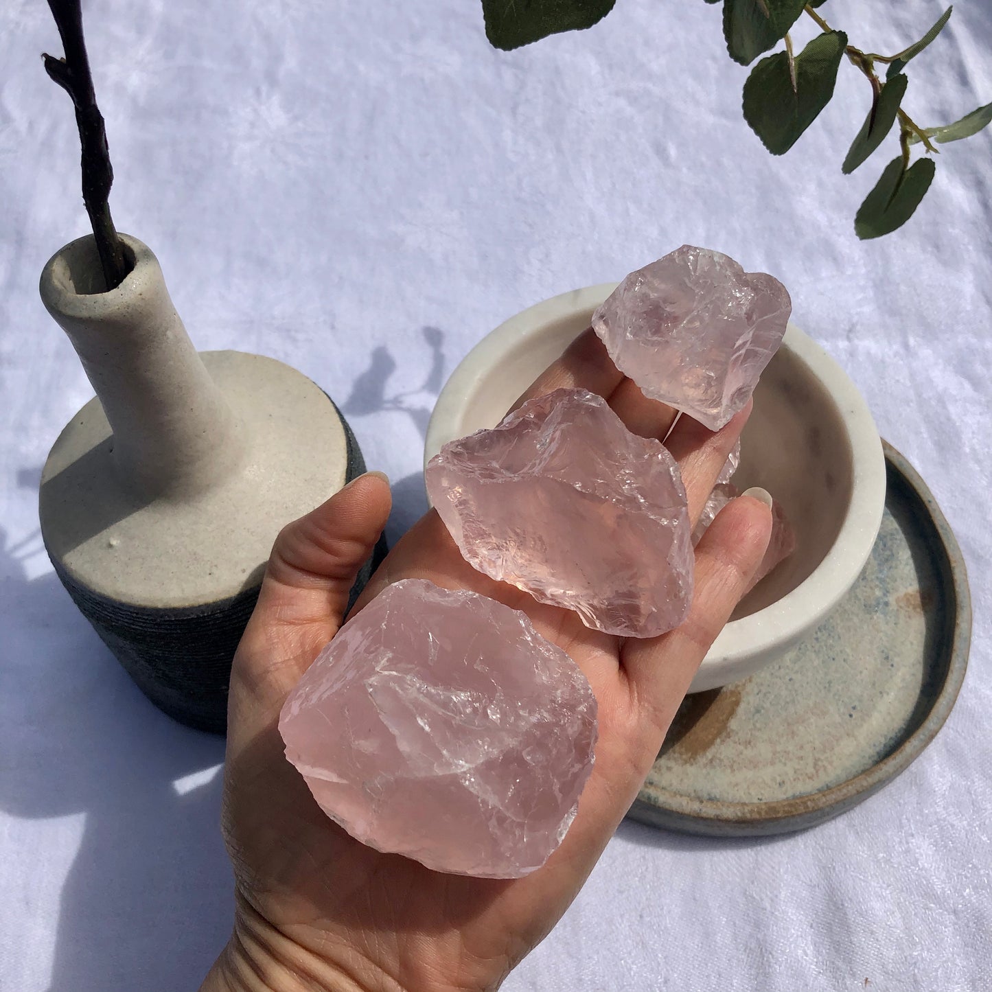 An open palm with three soft pink gems raw chunks of rose quartz crystal of descending sizes on it