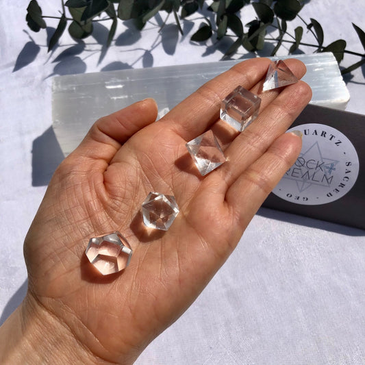 5 clear quartz geometric shapes held in the sun