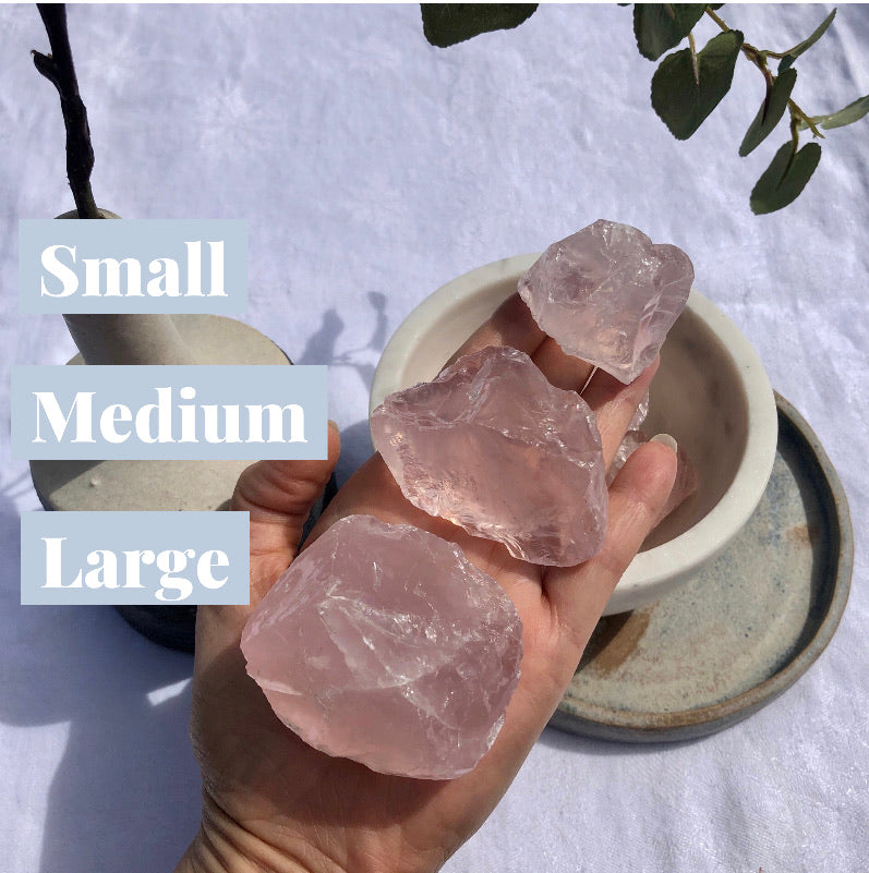 An open palm with three soft pink gems raw chunks of rose quartz crystal of descending sizes on it