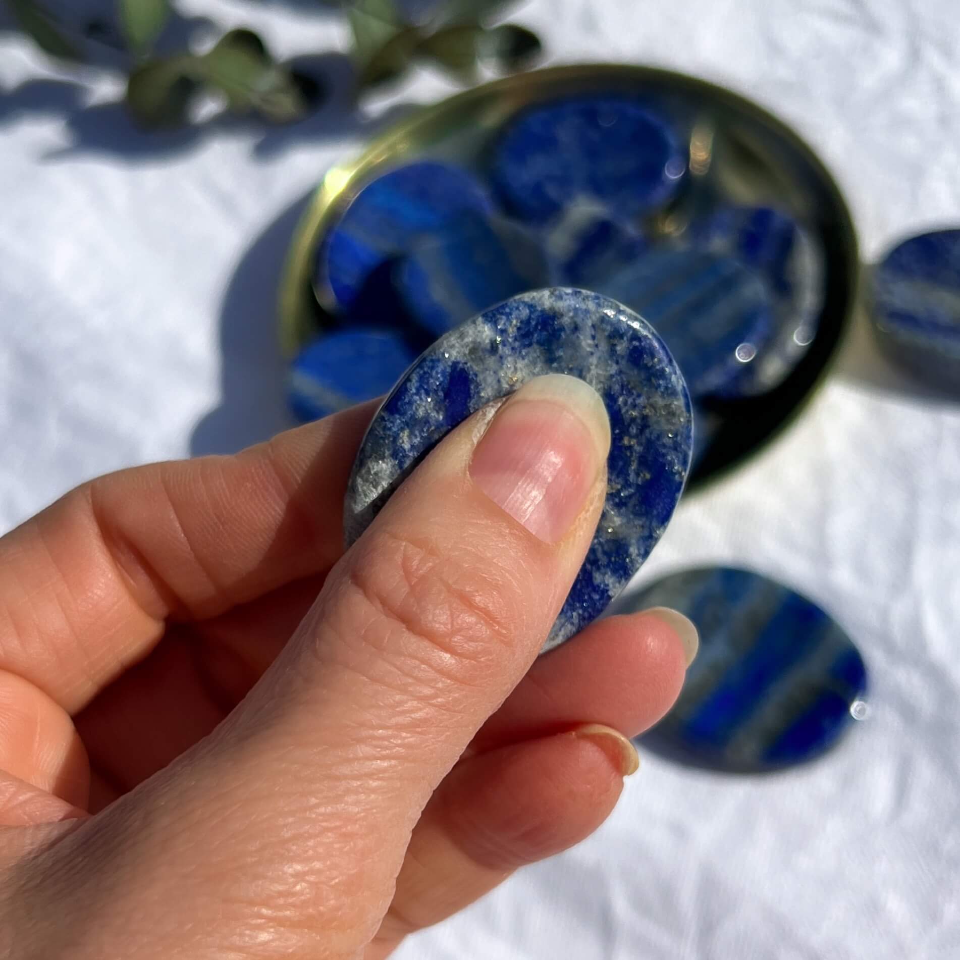 Royal blue, white and gold round Lapis Lazuli crystal worry stone pinched between a thumb and fingers