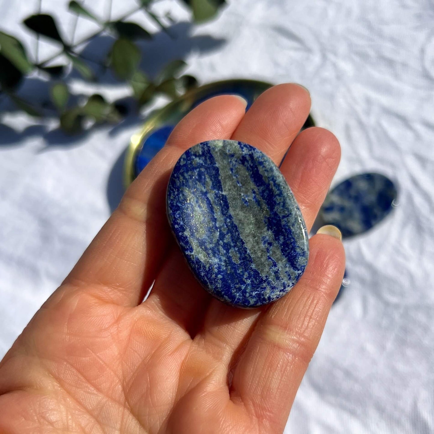 Royal blue, white and gold round Lapis Lazuli crystal worry stone lay flat in an open hand