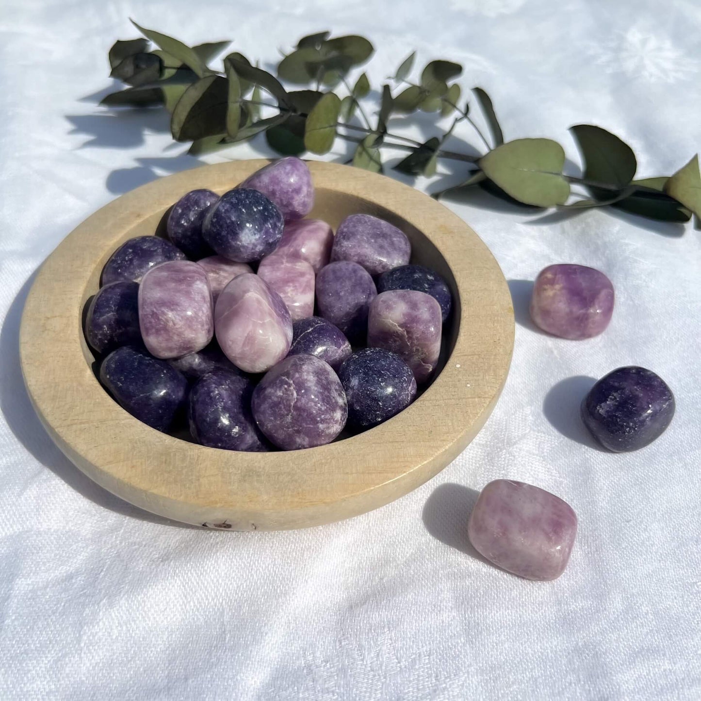 Dark and pale purple and white patterned lepidolite crystal tumblestones spilling from a wooden dish