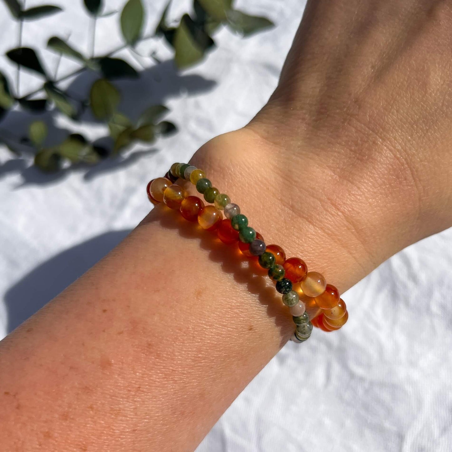 A lady's wrist with green and red healing crystal bead bracelets for courage; carnelian & green jasper