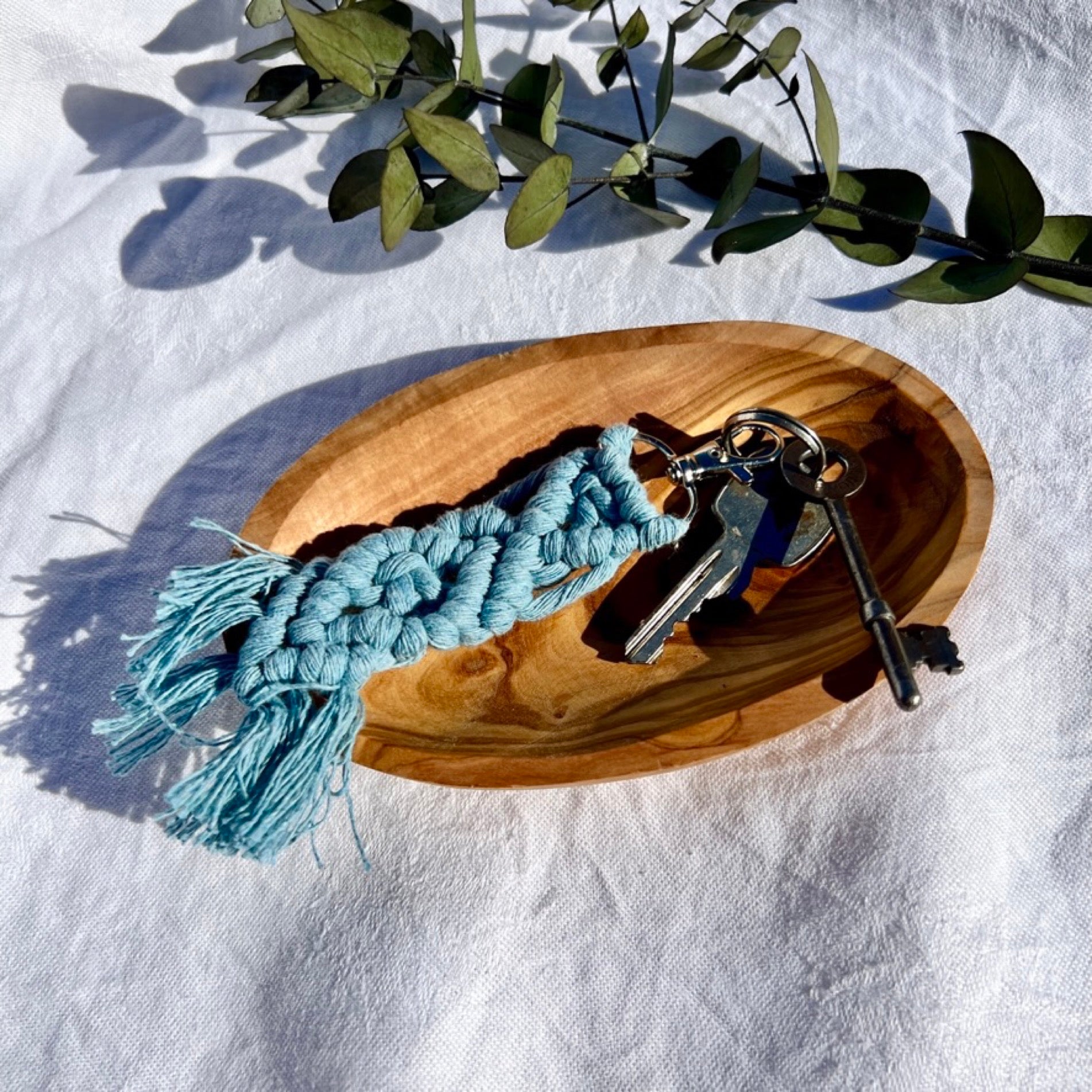 A blue macrame keyring sits in a honey coloured olive wood bowl
