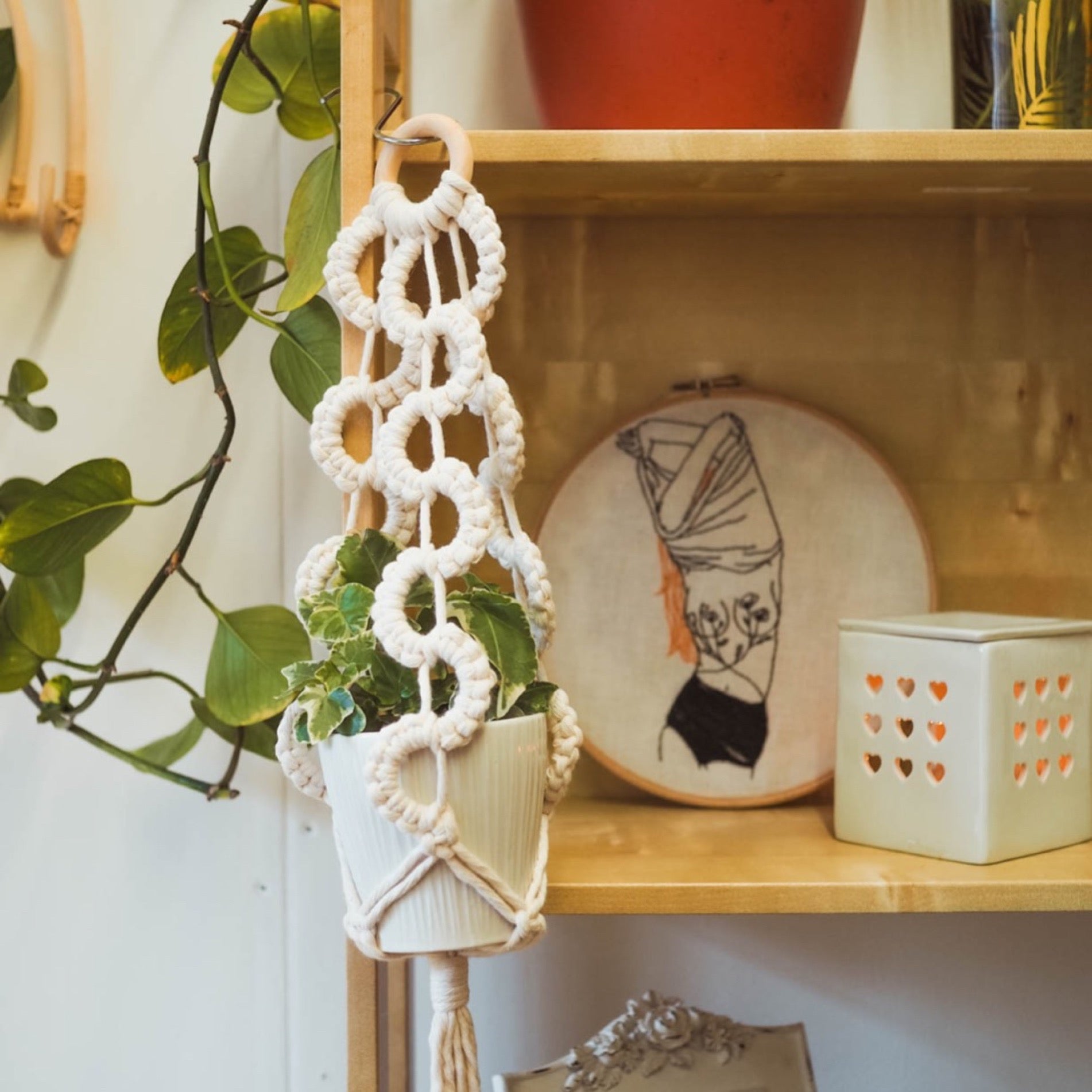 A wavy white macrame plant hanger hooked to shelves with cool boho ornaments on