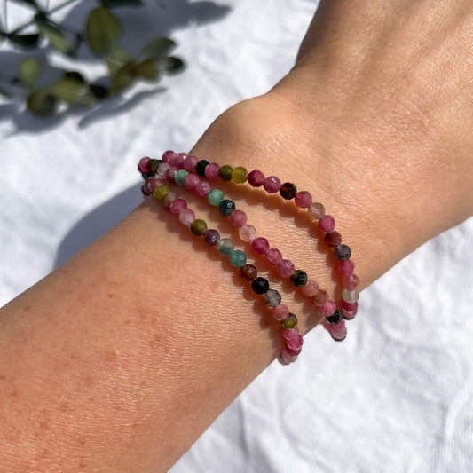 A lady's wrist with 3 multi-coloured pink, green & purple tourmaline crystal faceted bead bracelets