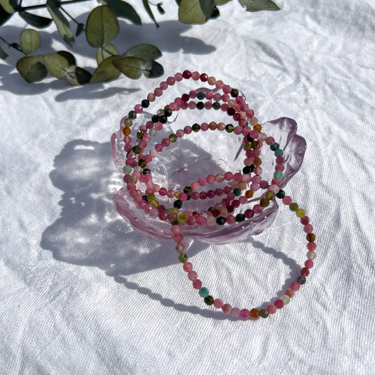 A glass dish filled with multi-coloured pink, green & purple tourmaline crystal faceted bead bracelets