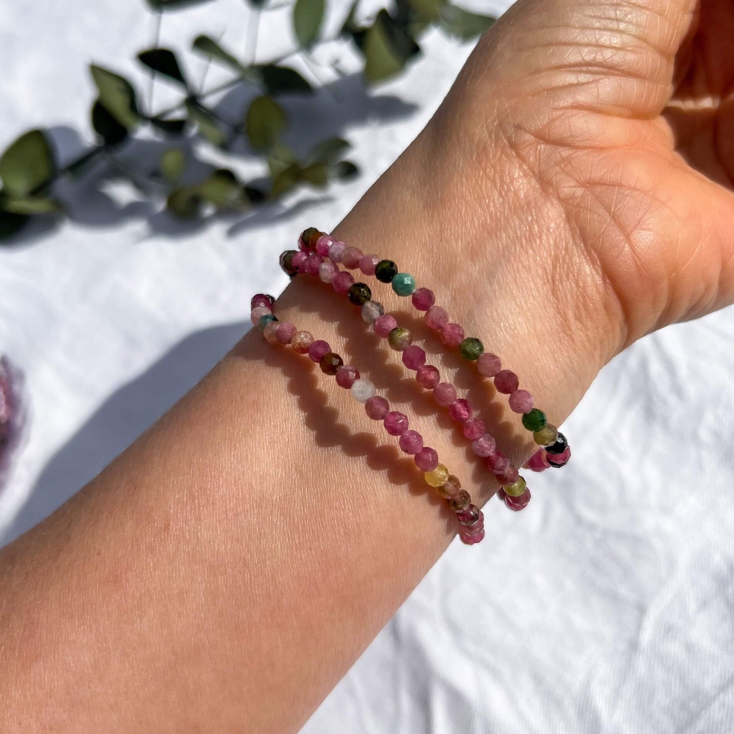 The underside of a woman's wrist with 3 multi-coloured pink, green & purple tourmaline crystal faceted bead bracelets