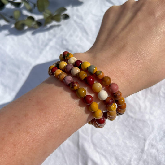 A woman's wrist wearing three red, orange & pink Mookaite healing crystal bead bracelets