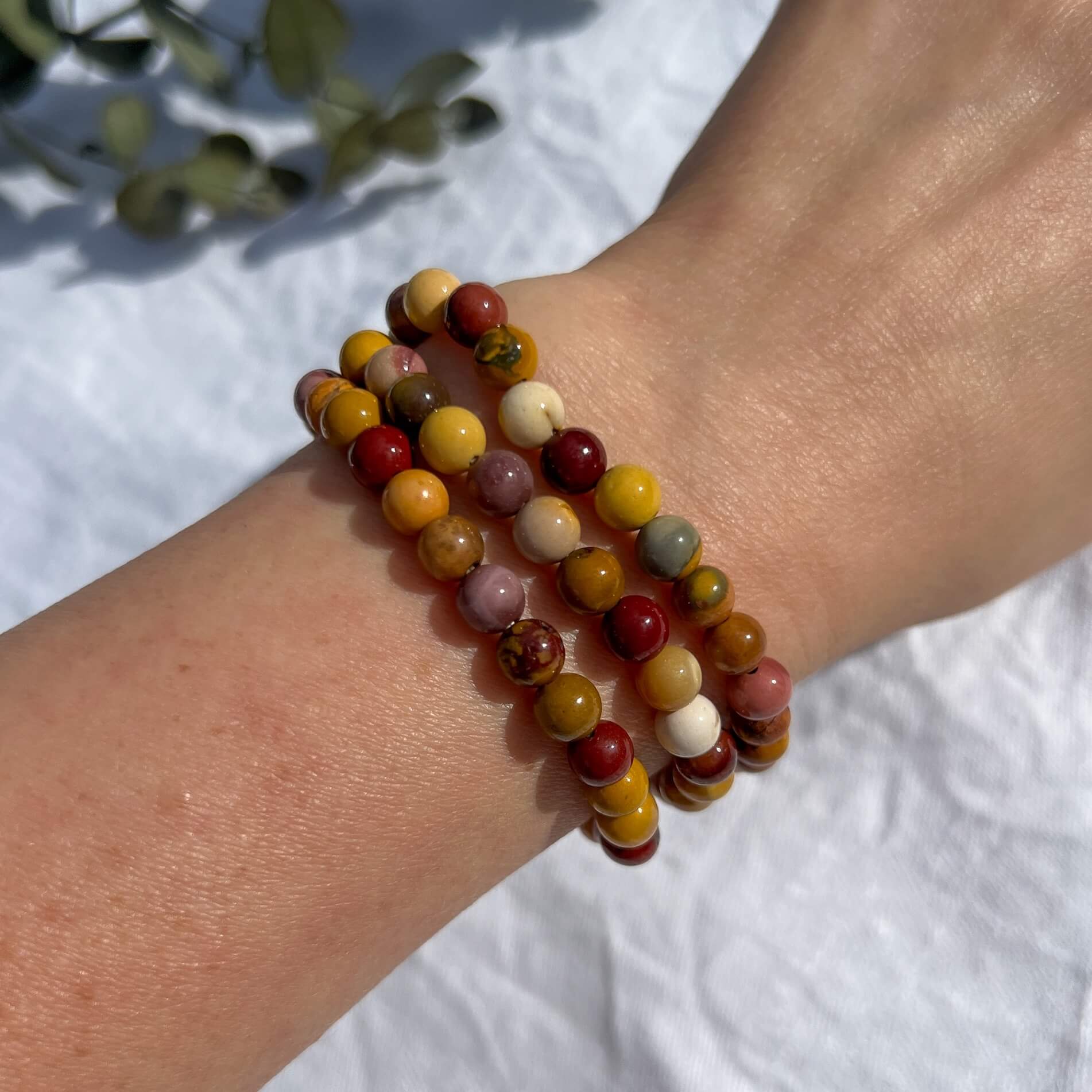 A lady's arm wearing three red, orange & pink Mookaite energising crystal bead bracelets