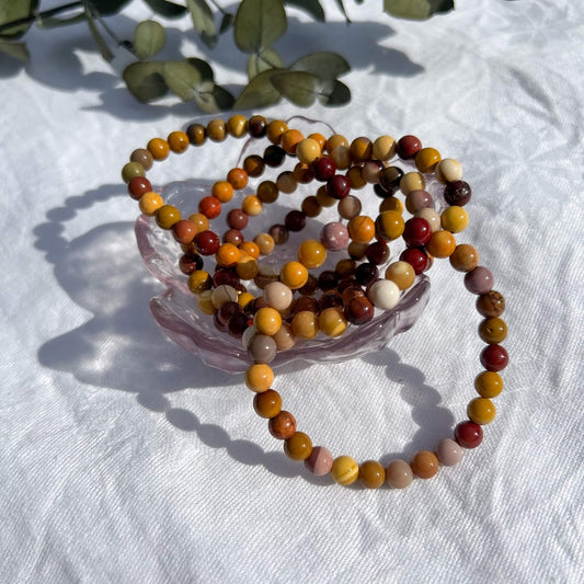 A glass trinket dish filled with red, orange & pink Mookaite healing crystal bead bracelets