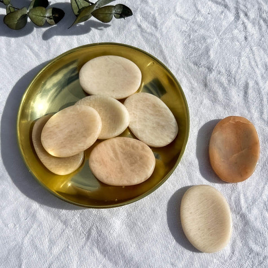 Peach moonstone disc shaped crystal worry stones in a brass dish