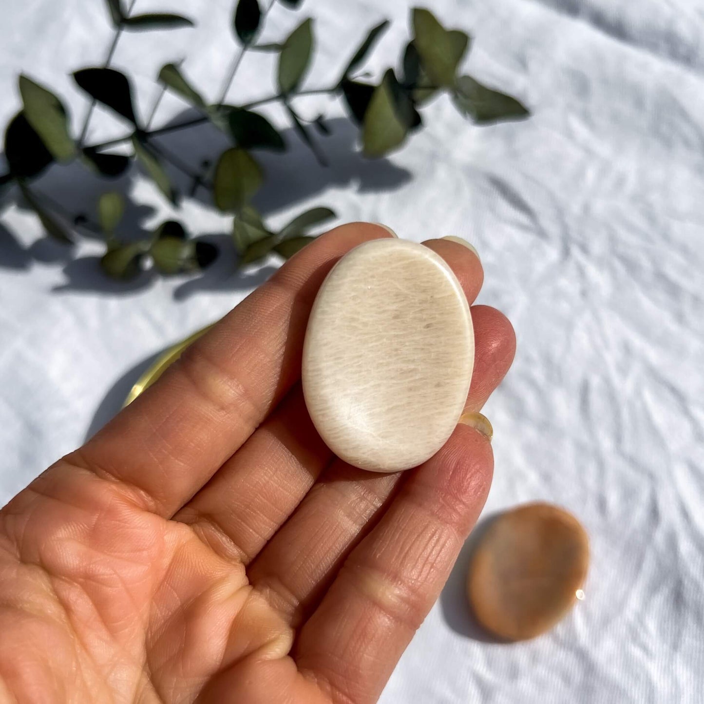 Peach moonstone disc shaped crystal thumb stone in an outstretched hand