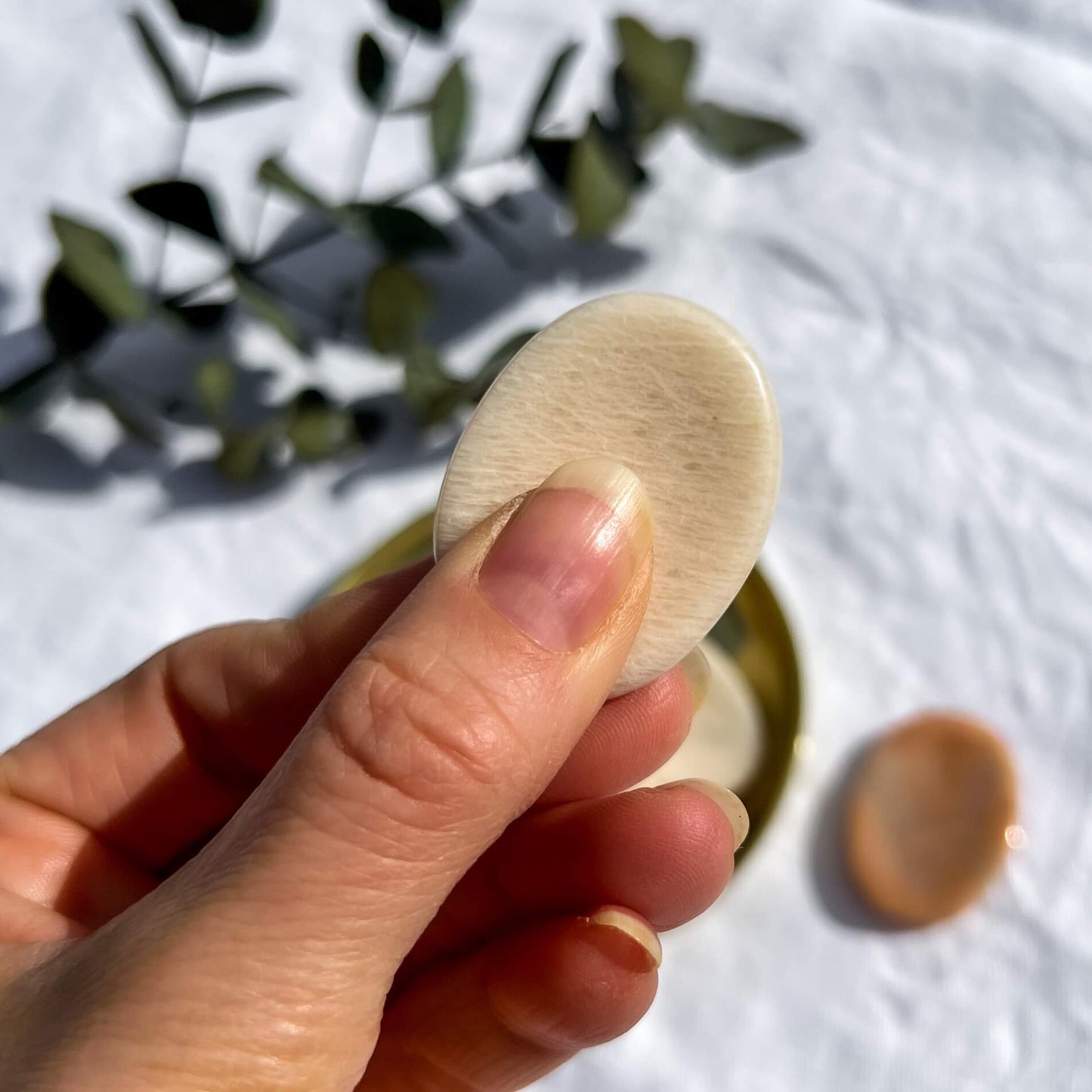 Peach moonstone disc shaped crystal worry stone pinched between thumb and fingers