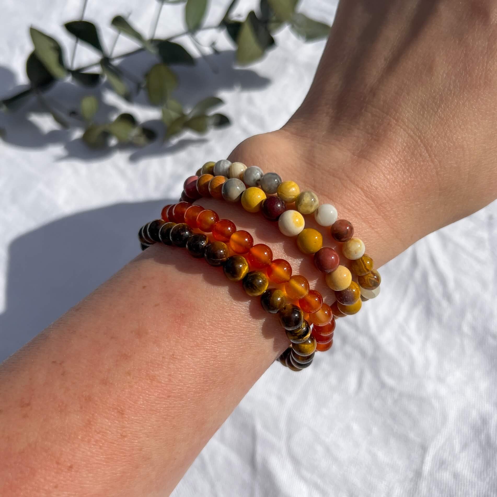 A woman's wrist wearing four energising crystal bead bracelets in tiger's eye, carnelian, mookaite and crazy lace agate